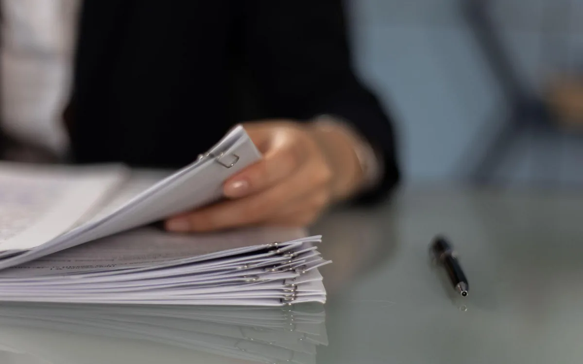 A person reviewing a stack of collision report paperwork on a desk