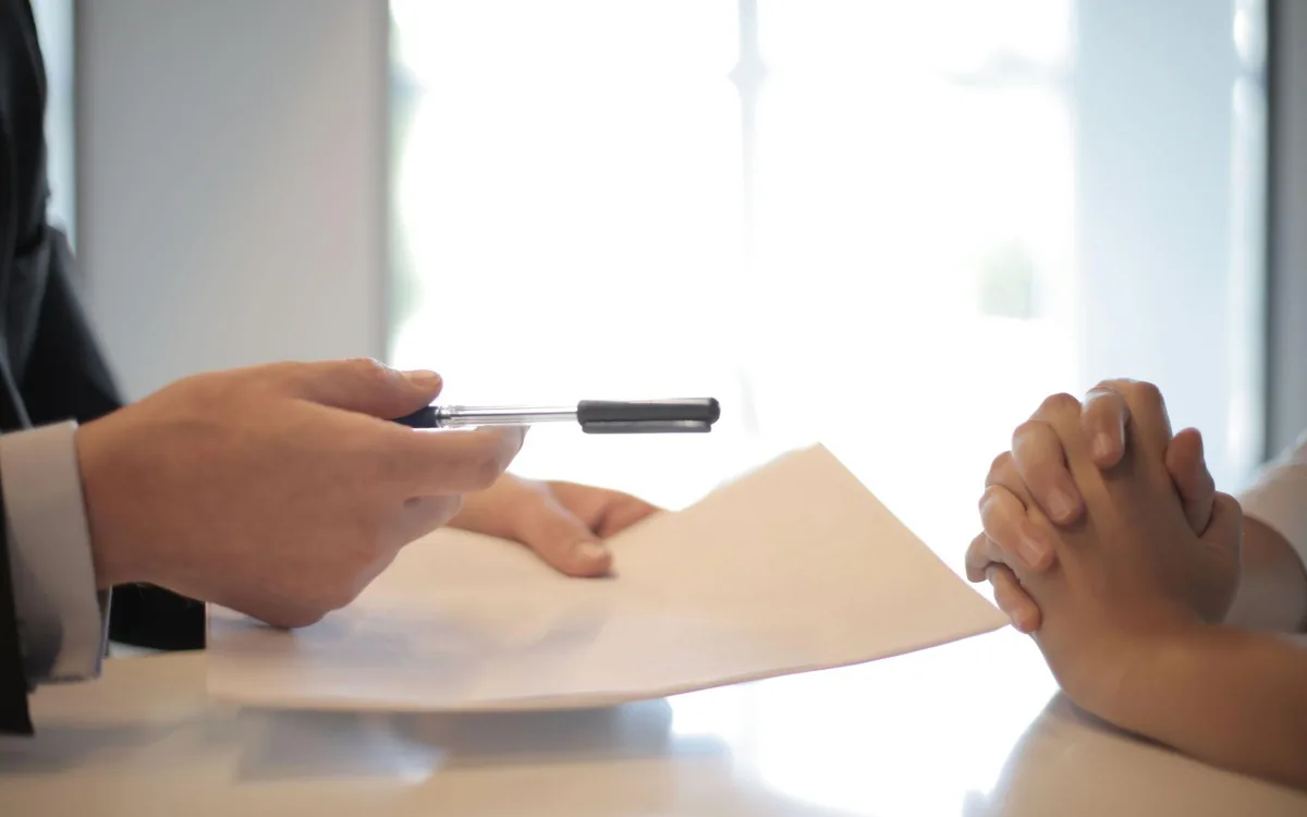 An insurance adjuster passing paperwork across a desk to a claimant